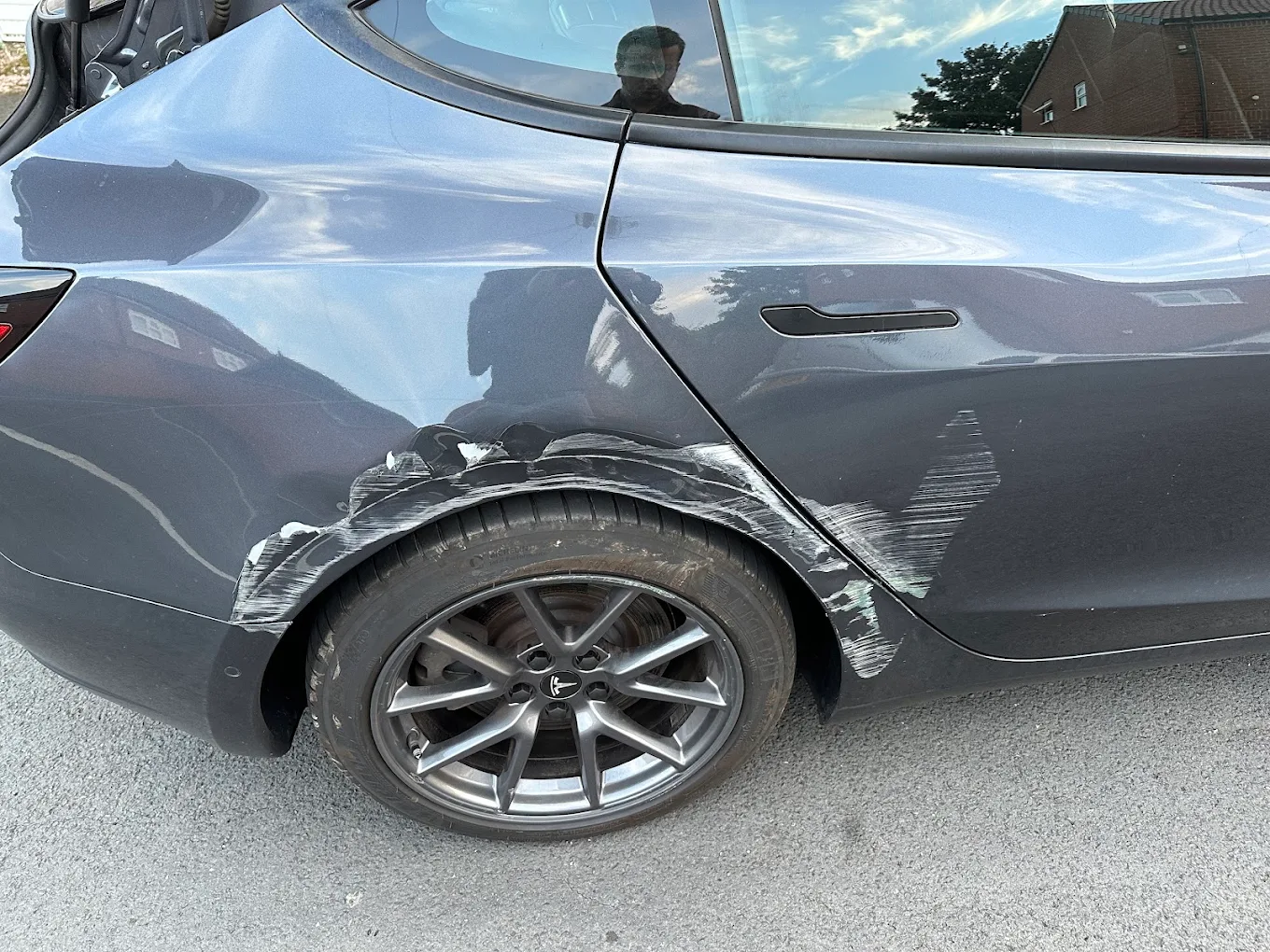 Grey Tesla with scuffs and panel damage around the rear wheel
